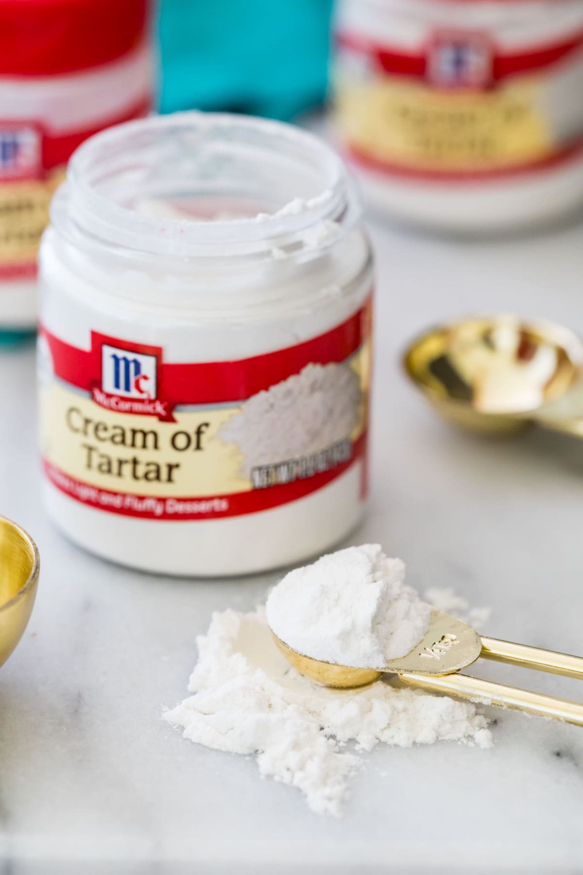 Small open jar of cream of tartar with a gold measuring spoon of cream of tartar beside it.
