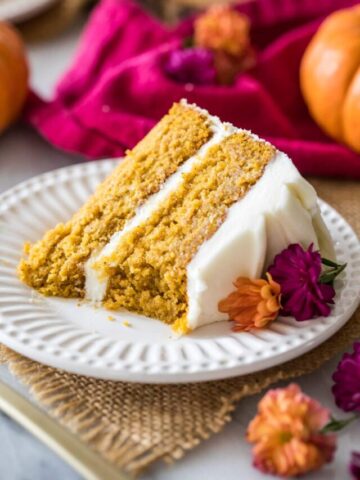Slice of pumpkin cake frosted with cream cheese frosting on a white plate.