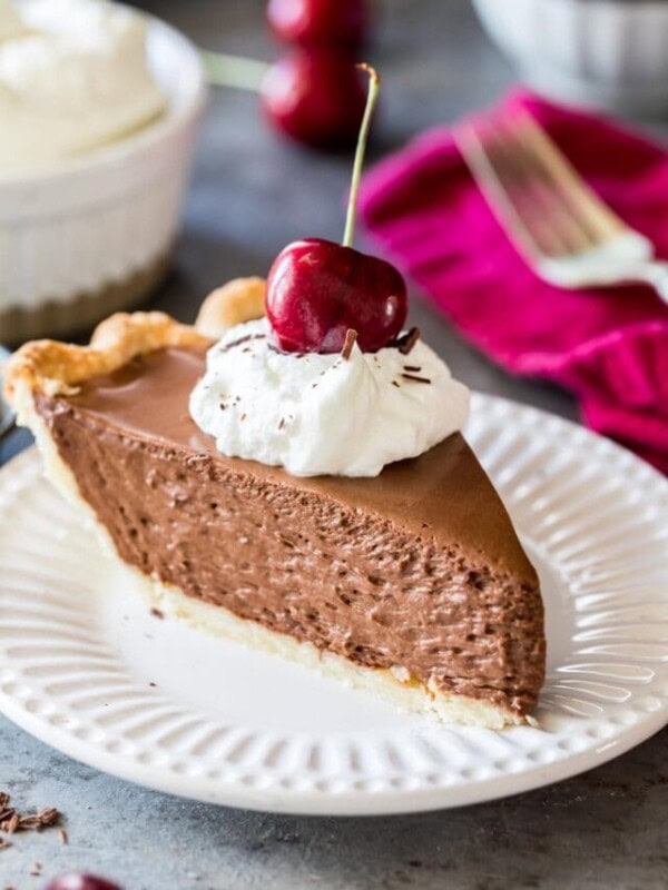 Slice of French silk pie topped with whipped cream and a sweet cherry served on a white plate.