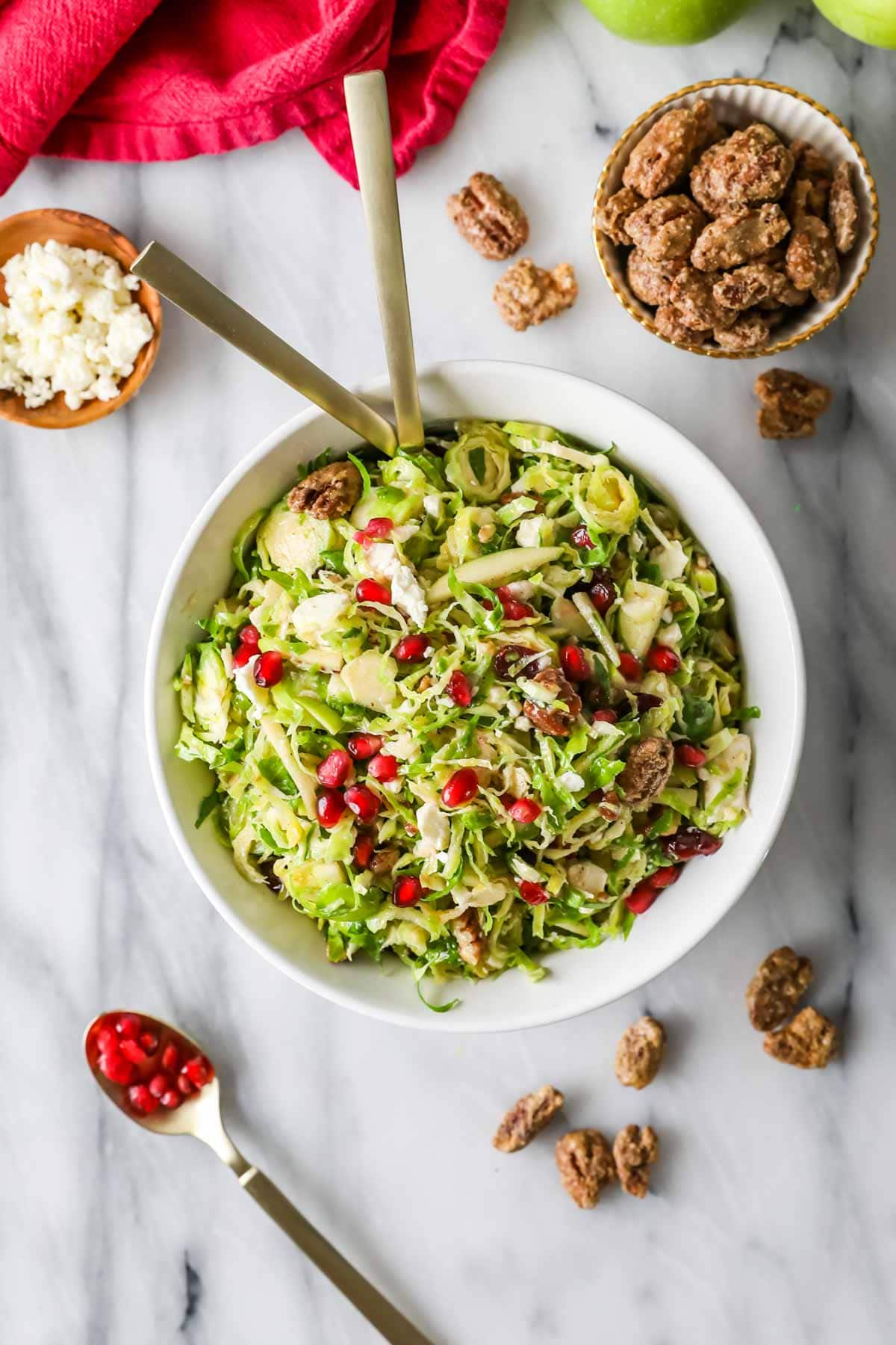 Overhead view of a white bowl of shaved brussels sprouts topped with nuts, cheese, and fruit to make a salad.