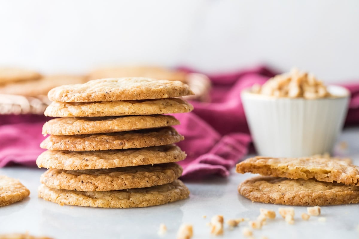 Golden brown cookies stacked next to a bowl of toffee chips and a half eaten cookie.