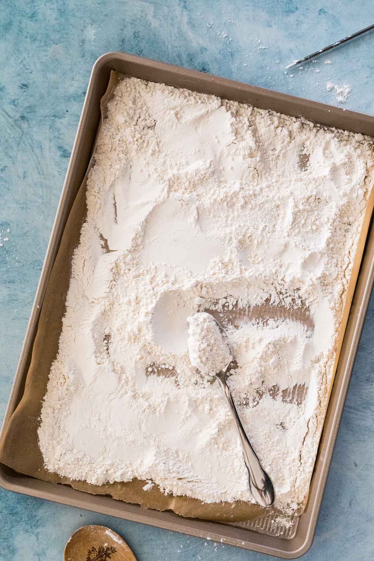Sheet pan of flour that's been stirred by a spoon.