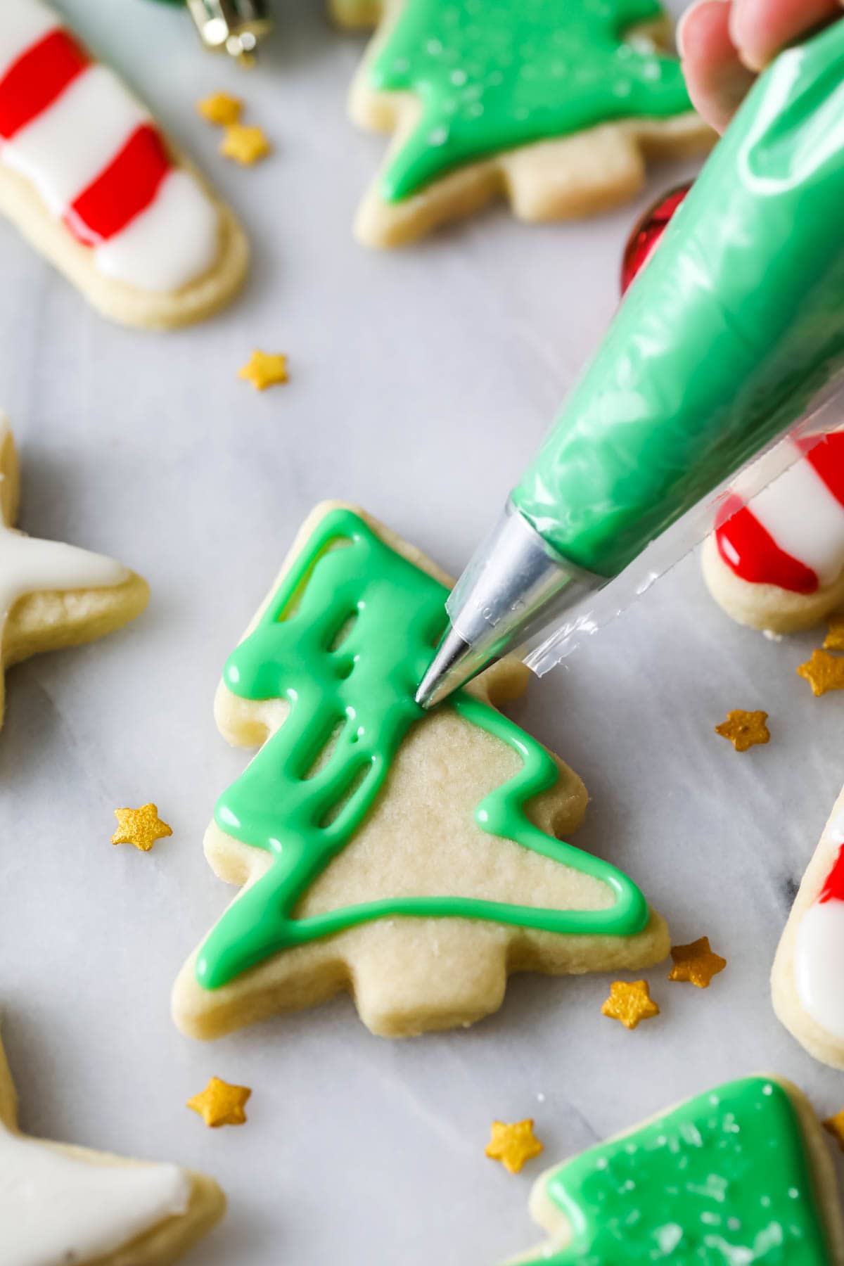 Green icing being piped onto a christmas tree shaped cookie.