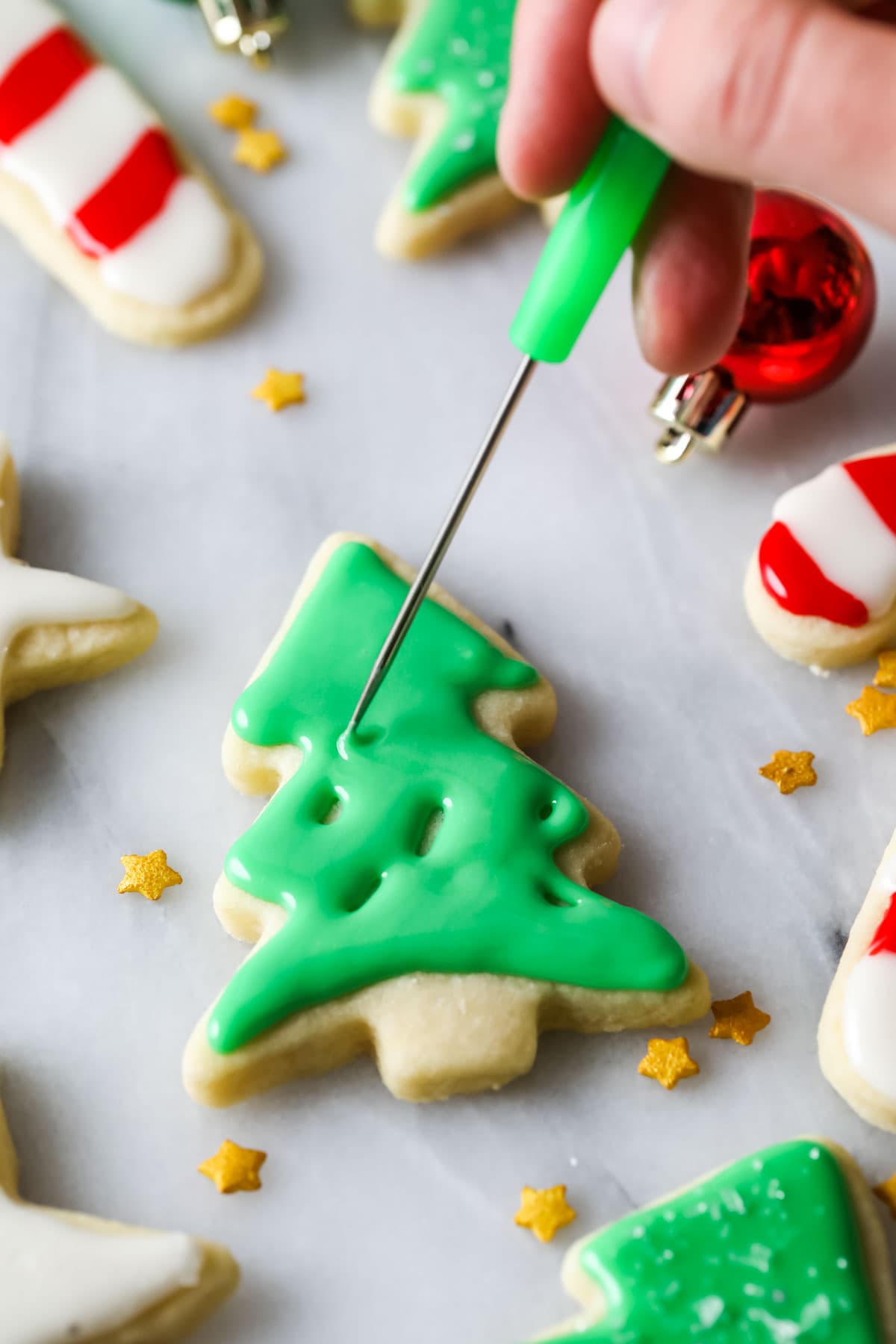 Stick tool smoothing out green icing on a christmas tree sugar cookie.