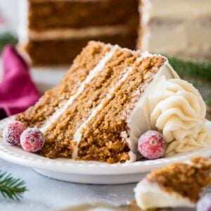 Slice of gingerbread layer cake topped with cream cheese frosting and sugared cranberries.
