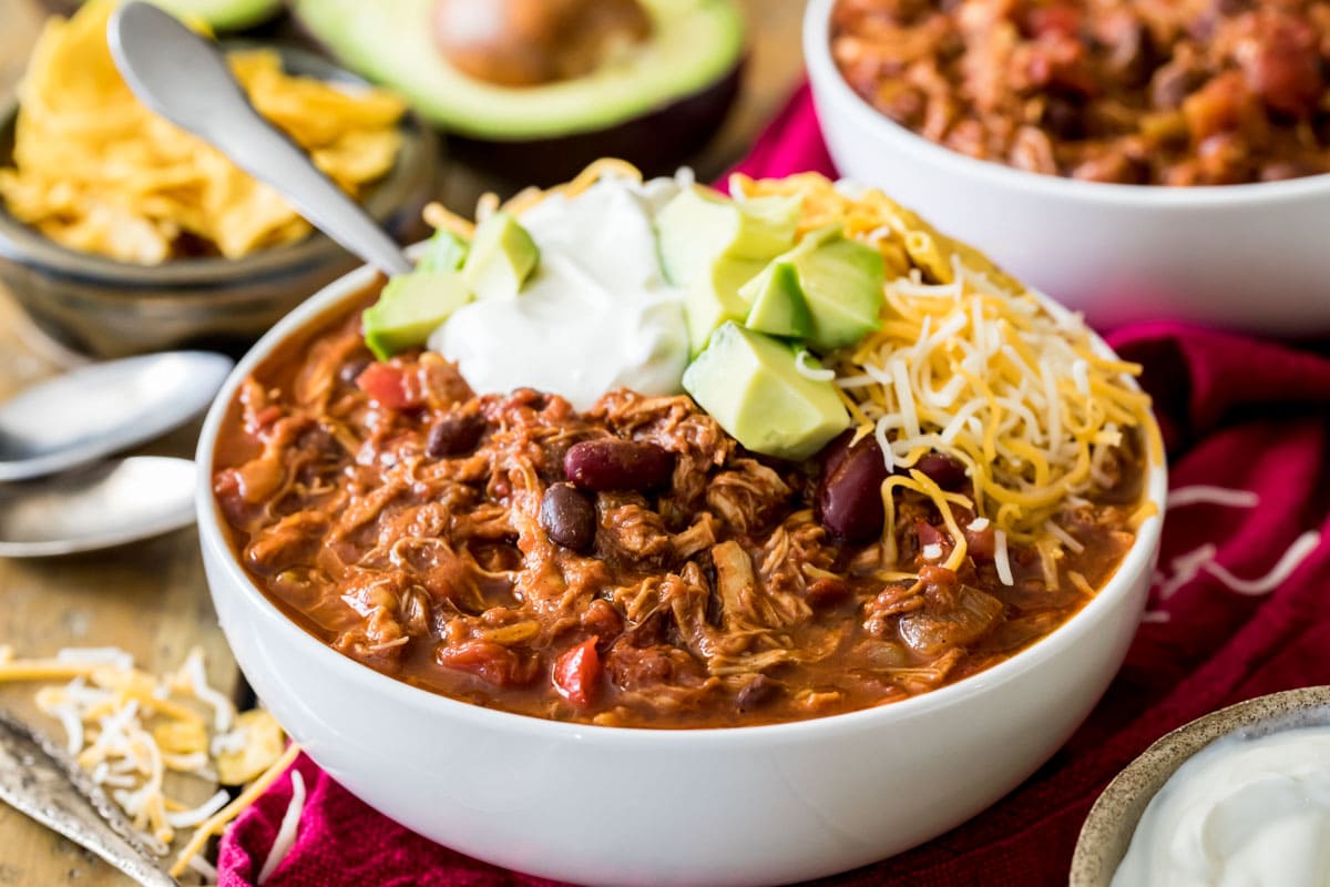 Bowl of chili topped with sour cream, avocado, and shredded cheese.