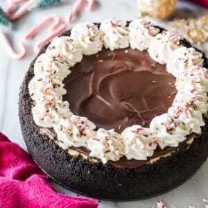 Overhead view of a peppermint bark cheesecake topped with chocolate ganache, whipped cream, and crushed peppermint candy.