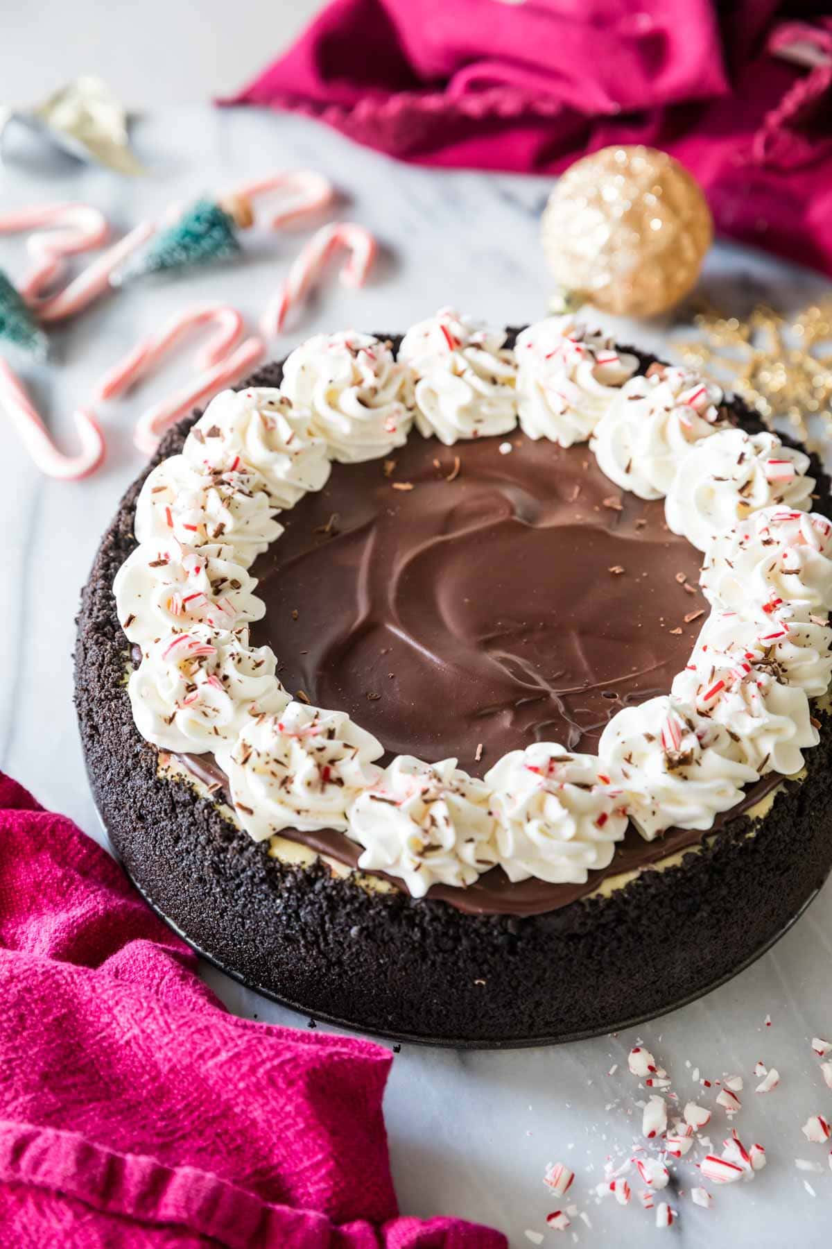 Overhead view of a peppermint bark cheesecake topped with chocolate ganache, whipped cream, and crushed peppermint candy.