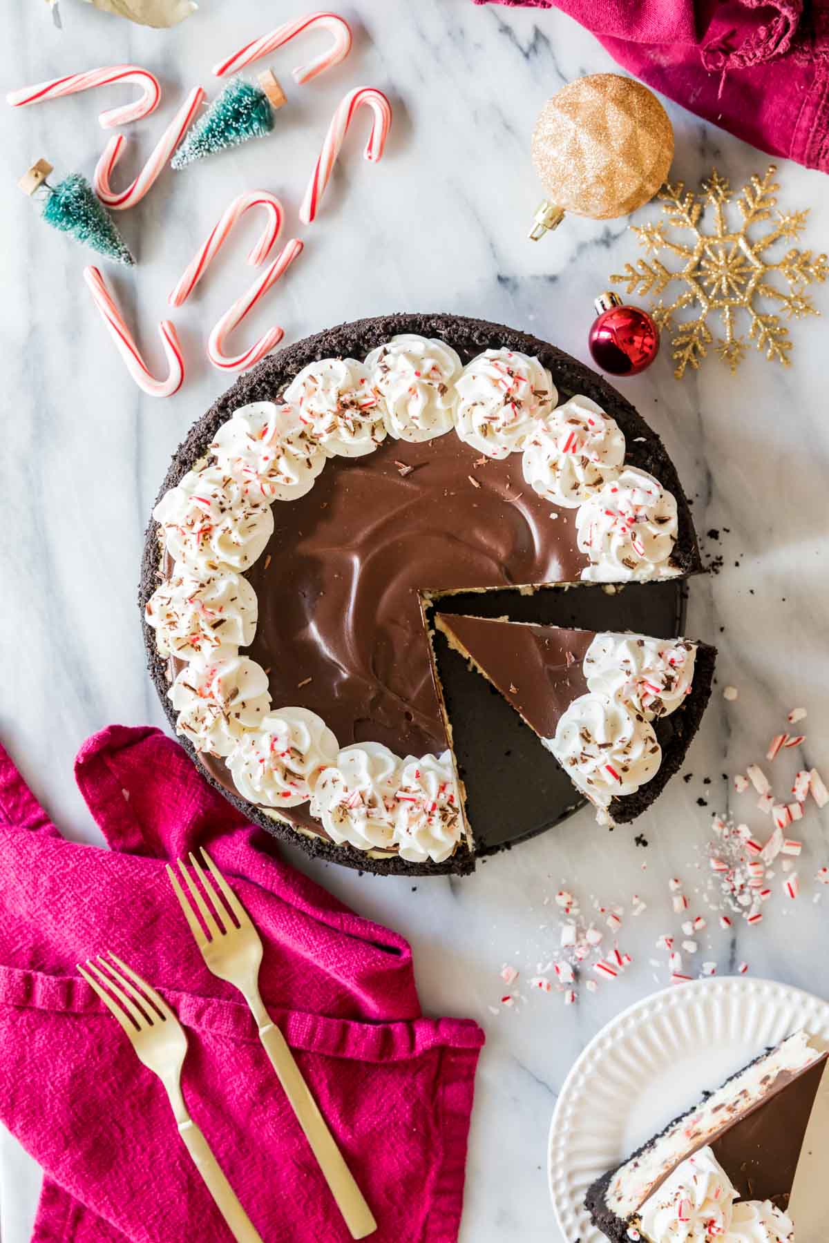 Overhead view of a cheesecake topped with chocolate ganache, whipped cream, and crushed peppermint candy.