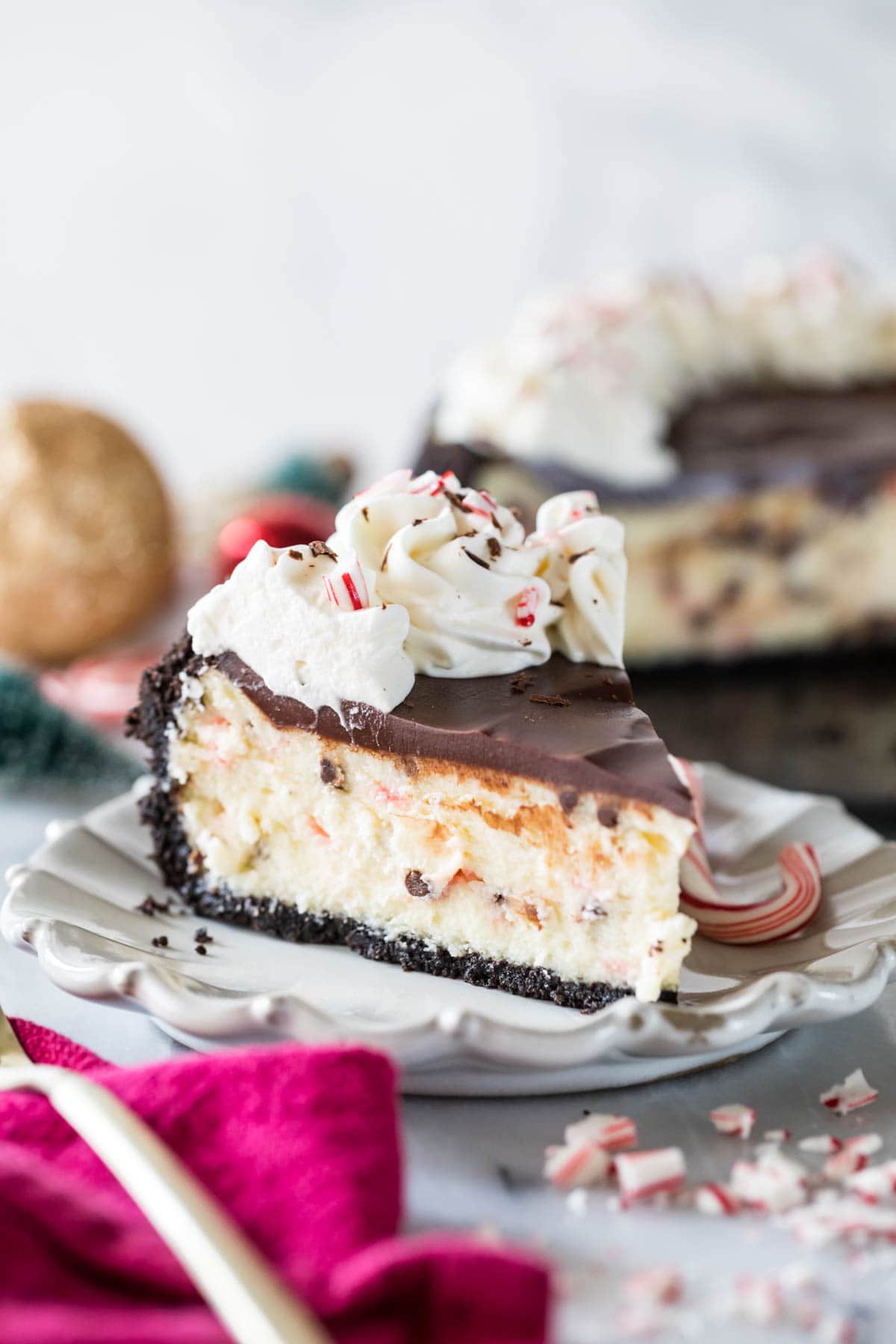 Slice of peppermint bark cheesecake topped with chocolate ganache, whipped cream, and crushed peppermint candy.