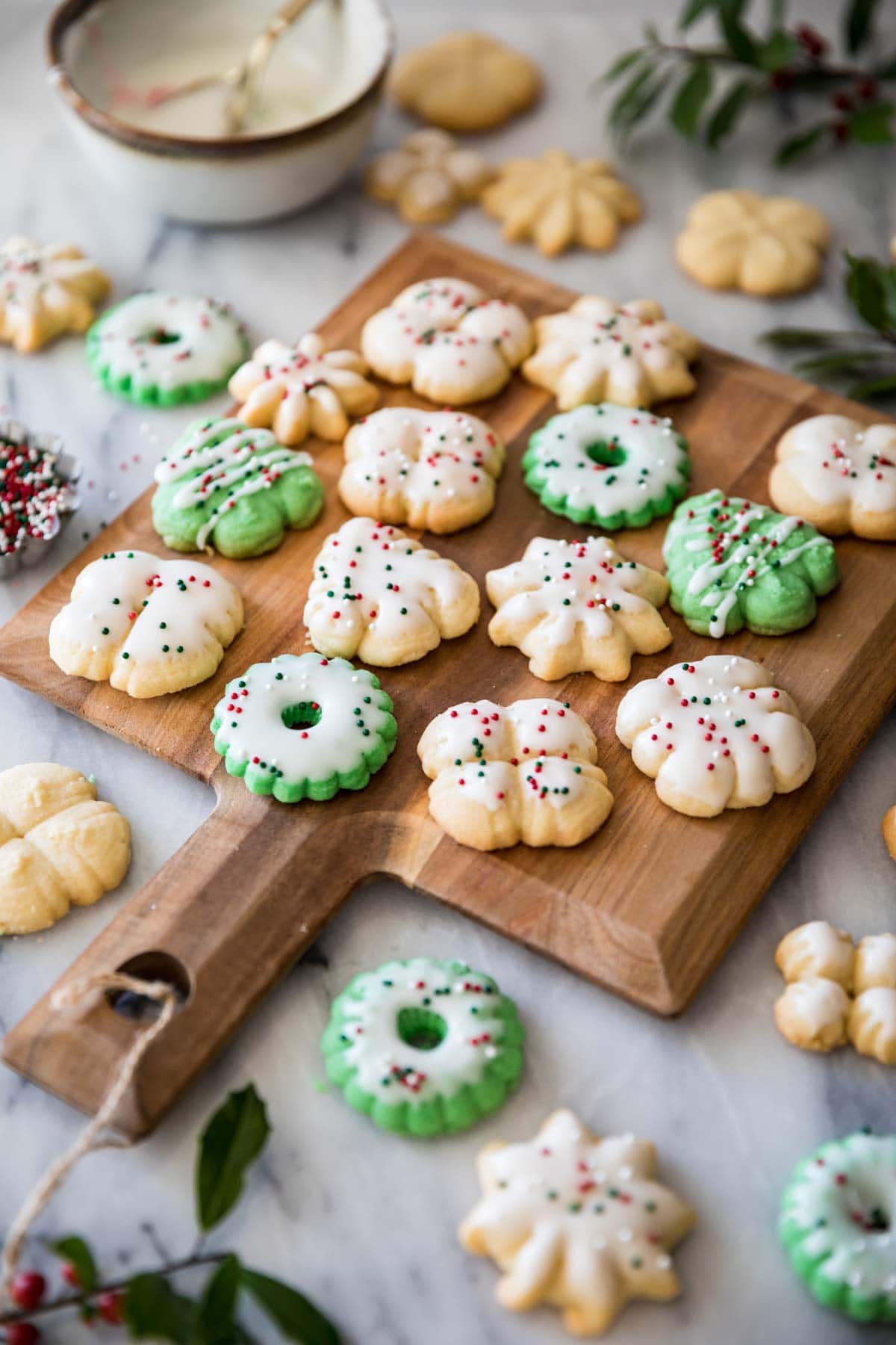 Colorful and festive spritz cookies shaped like wreaths, trees, and snowflakes on a wood cutting board.