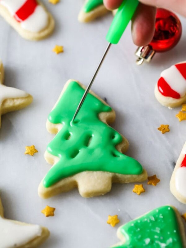 Stick tool smoothing out green icing on a christmas tree sugar cookie.