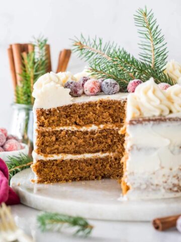 Cross section of a three layer cake topped with sugared cranberries and evergreen sprigs.