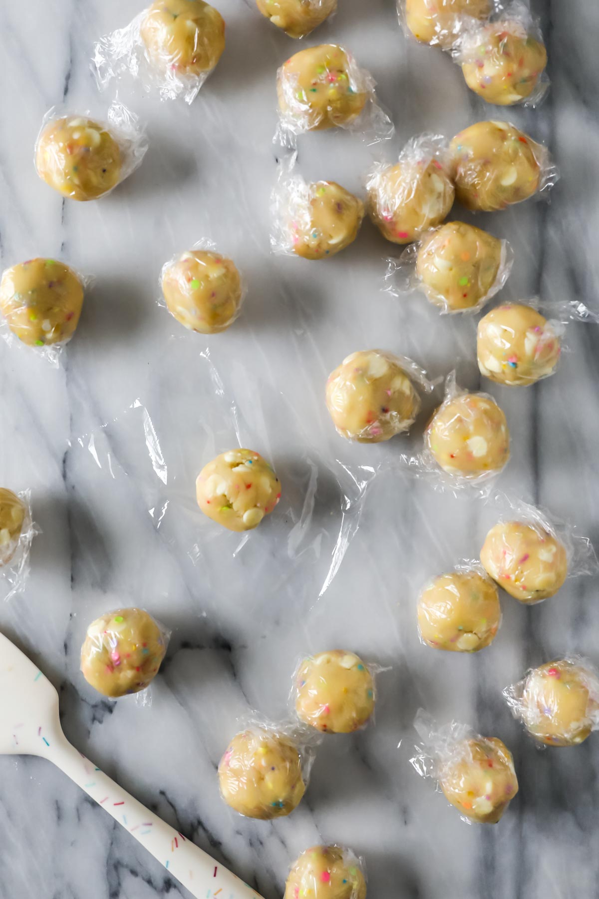 Cookie dough balls that have been wrapped in plastic in preparation for freezing.