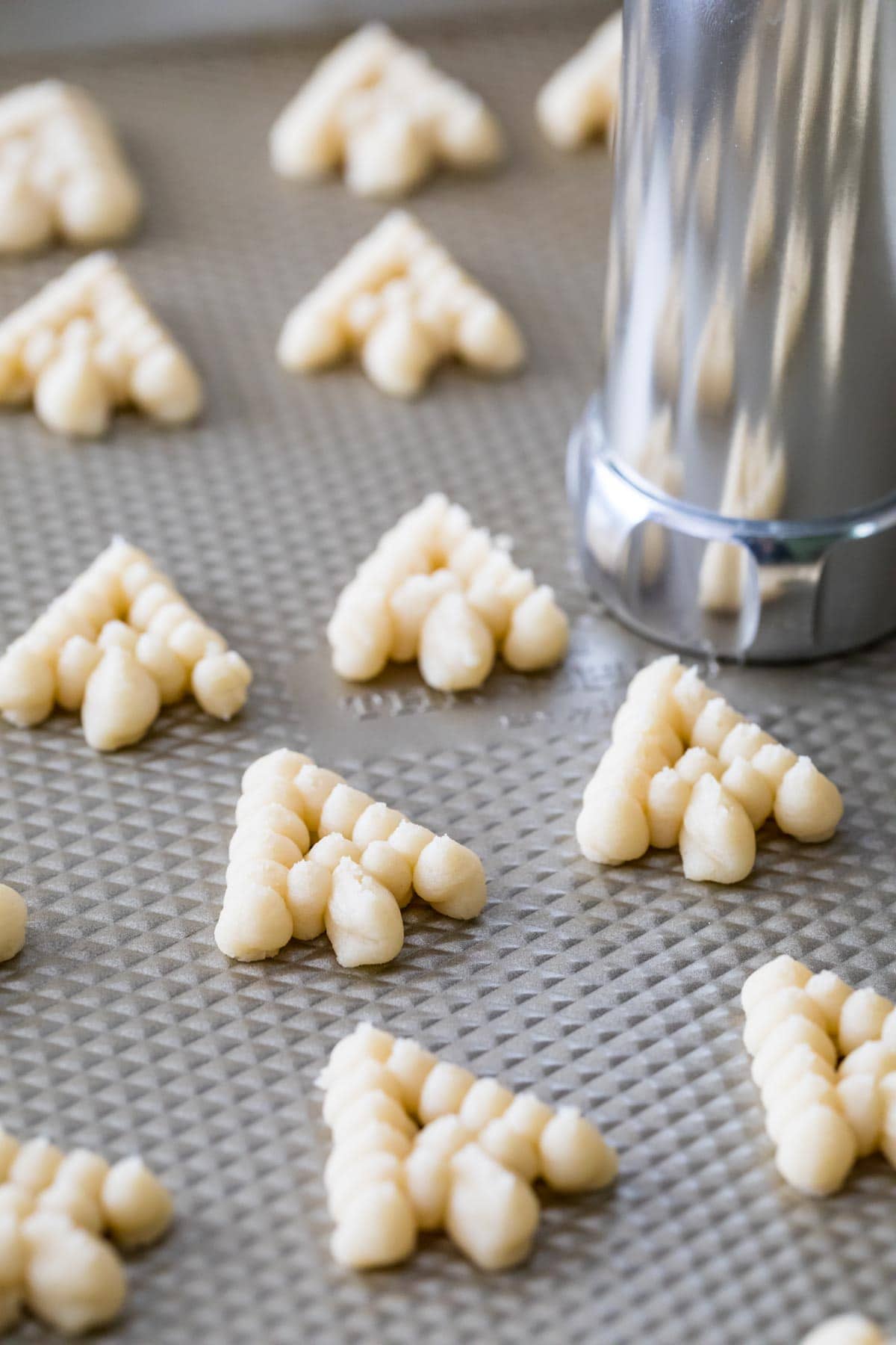 Cookie press pressing tree-shaped cookie dough onto a baking sheet.