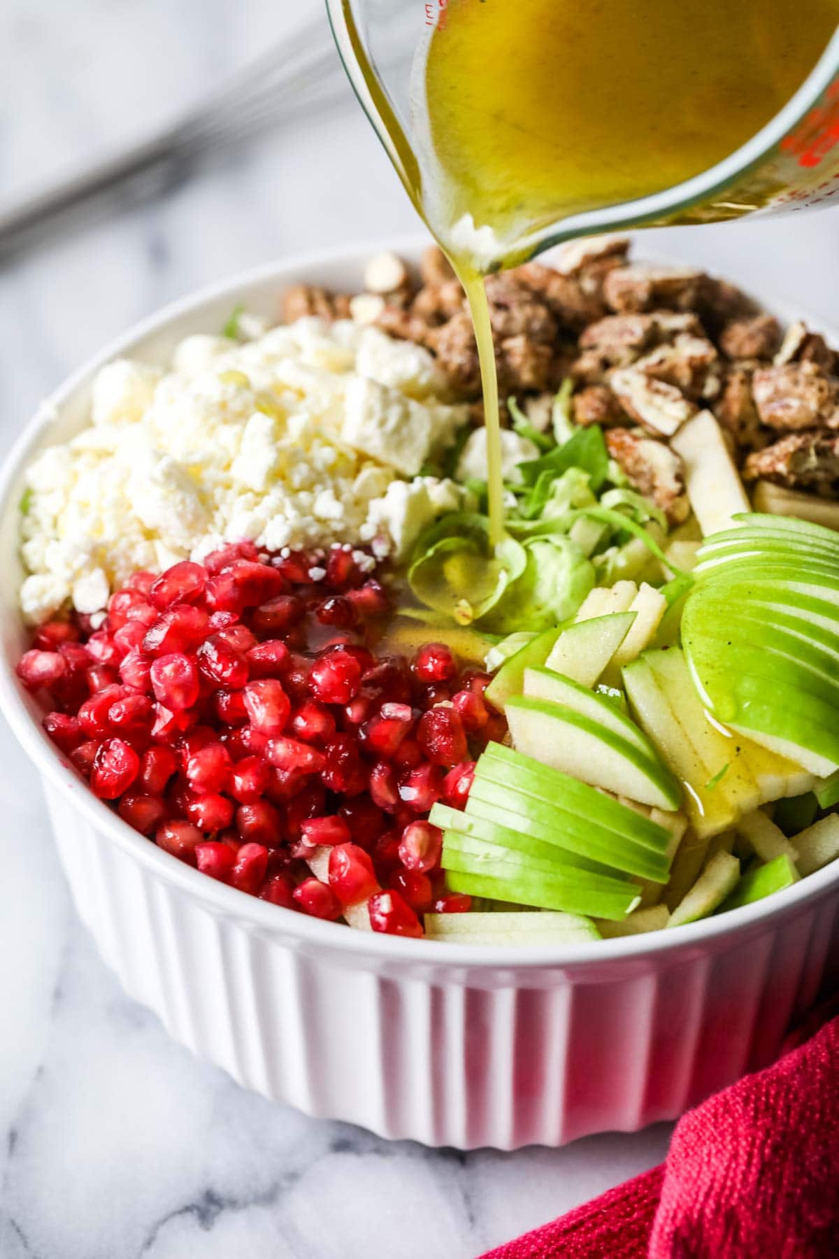 pouring vinaigrette dressing over brussels sprouts salad ingredients in a white bowl