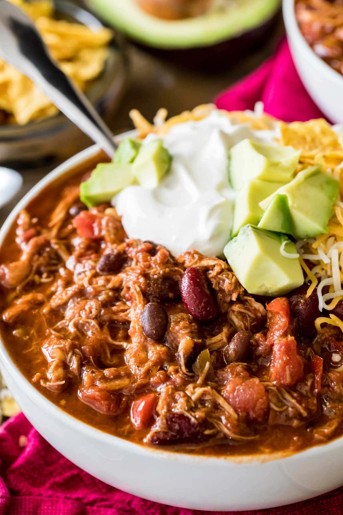 Bowl of chili topped with sour cream, avocado, and shredded cheese.