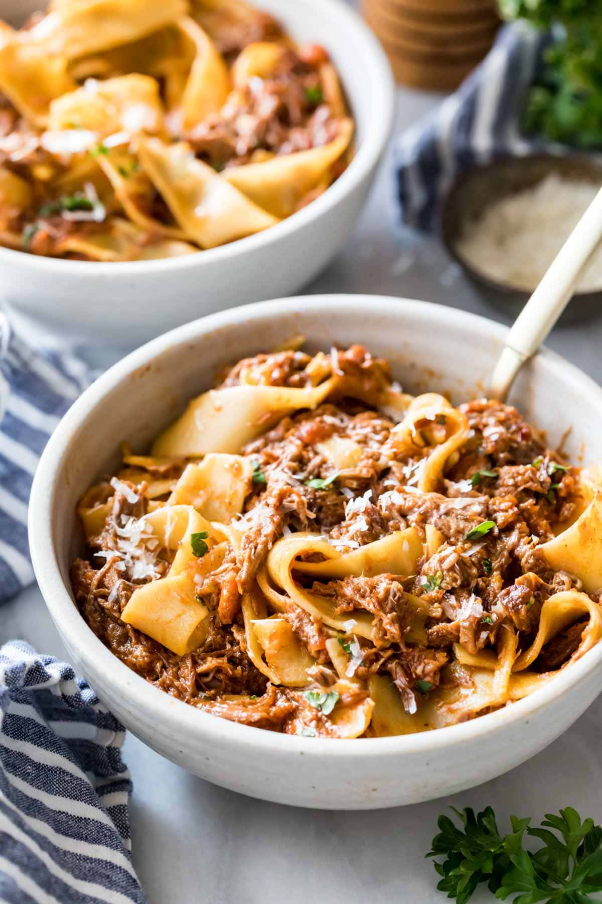 Two bowls of wide, long pasta noodles tossed in a shredded beef and tomato sauce.