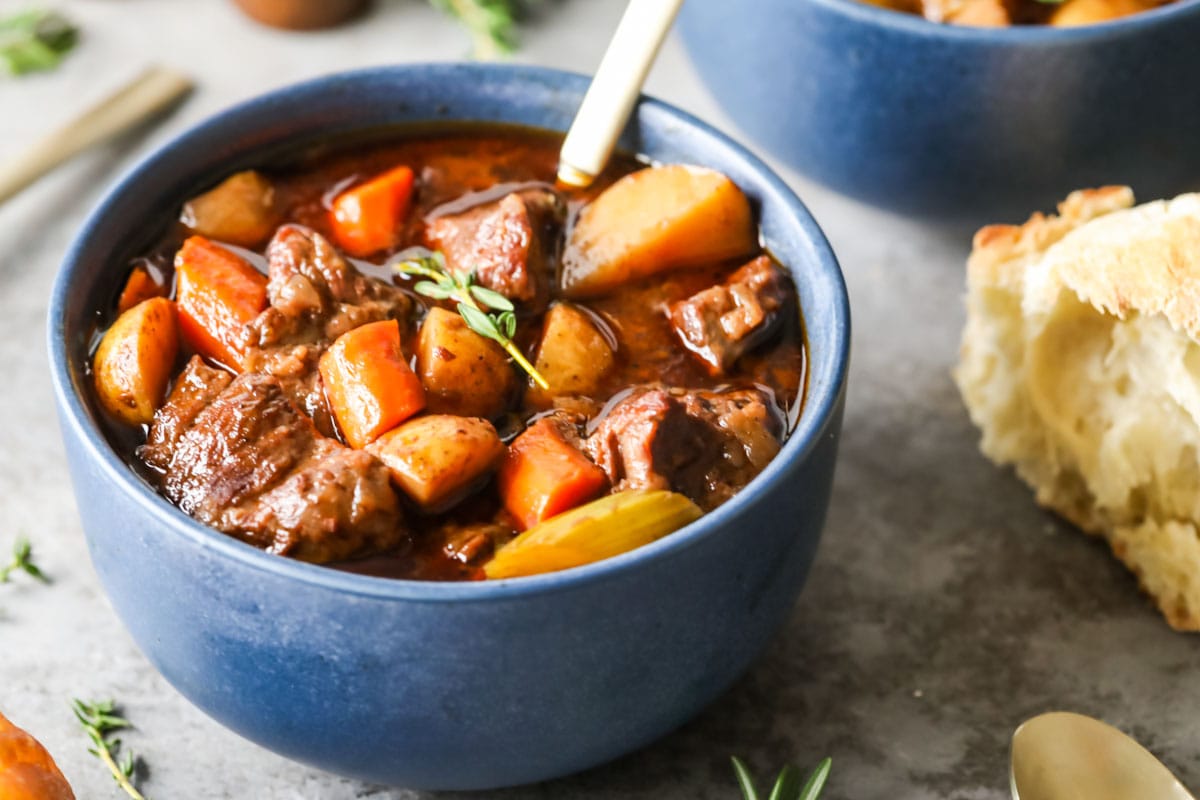 Blue bowl of stew made with potatoes, carrots, and beef.