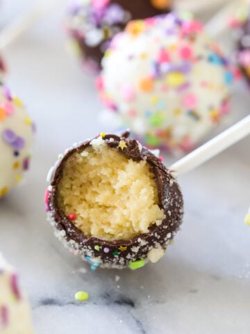Chocolate covered cake pop bitten to show a yellow cake filling surrounded by other cake pops.