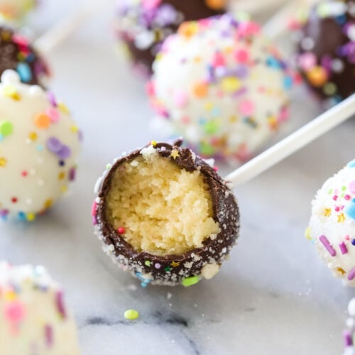 Chocolate covered cake pop bitten to show a yellow cake filling surrounded by other cake pops.