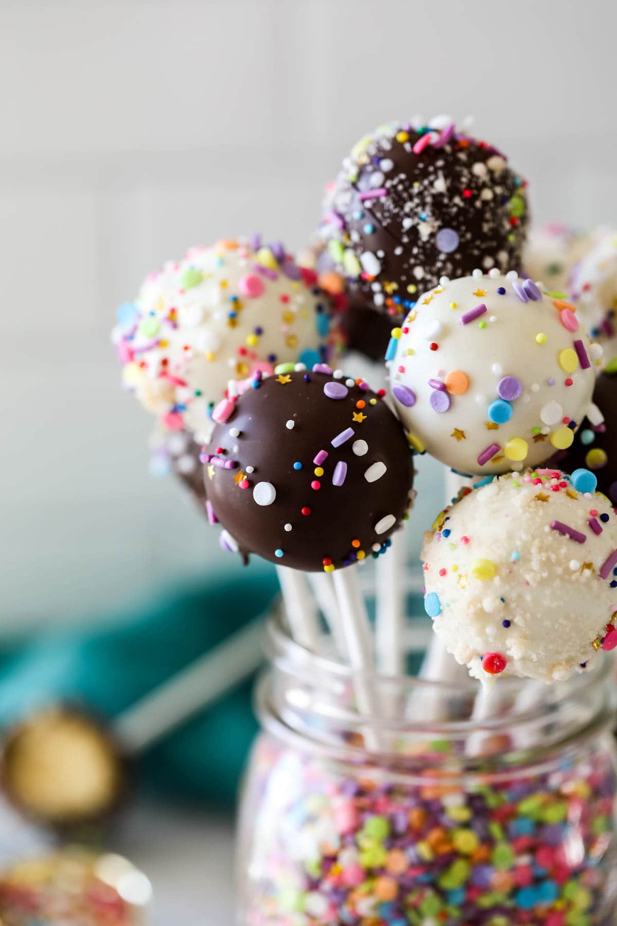 Glass jar with chocolate and sprinkle coated cake balls on sticks.