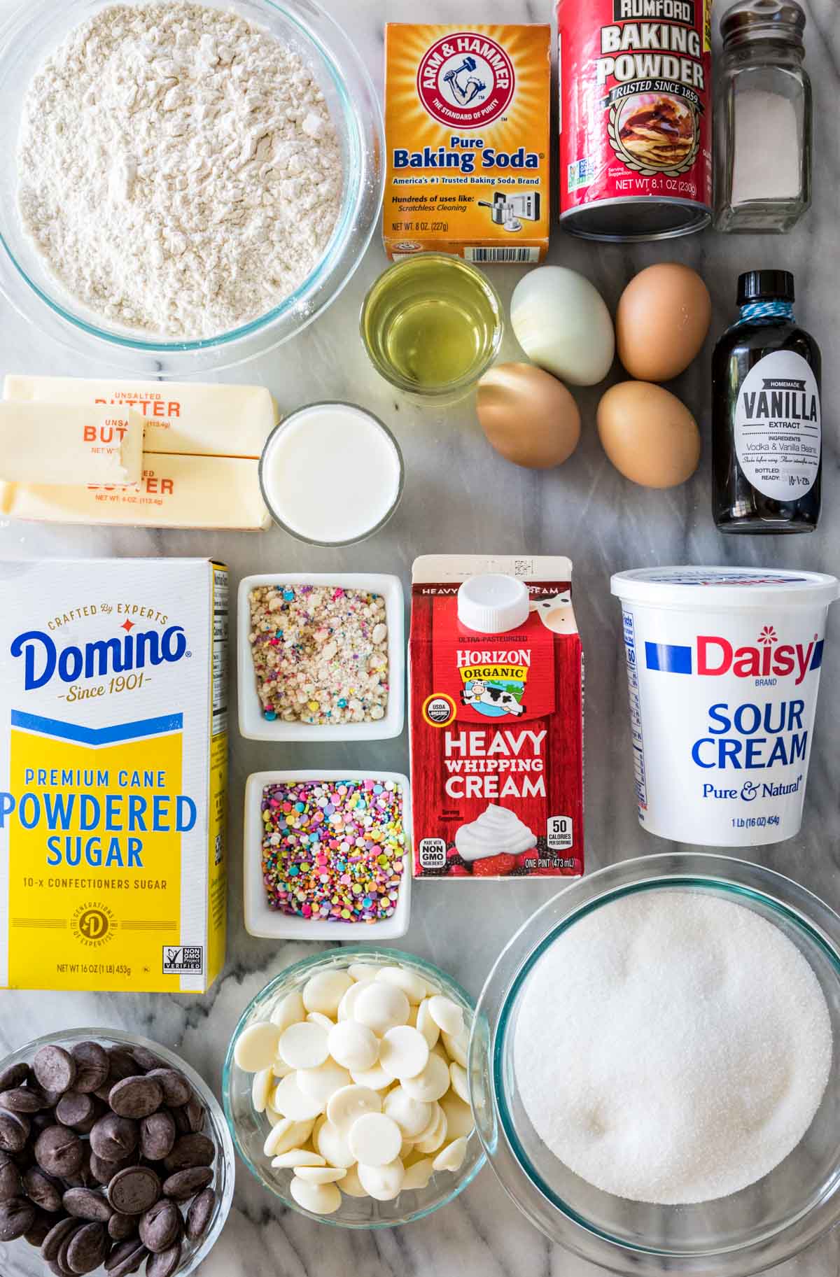Overhead view of ingredients including flour, butter, powdered sugar, sprinkles, sour cream, and more.