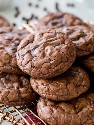 Crinkly-topped flourless chocolate cookies stacked in a pile on a metal cooling rack.