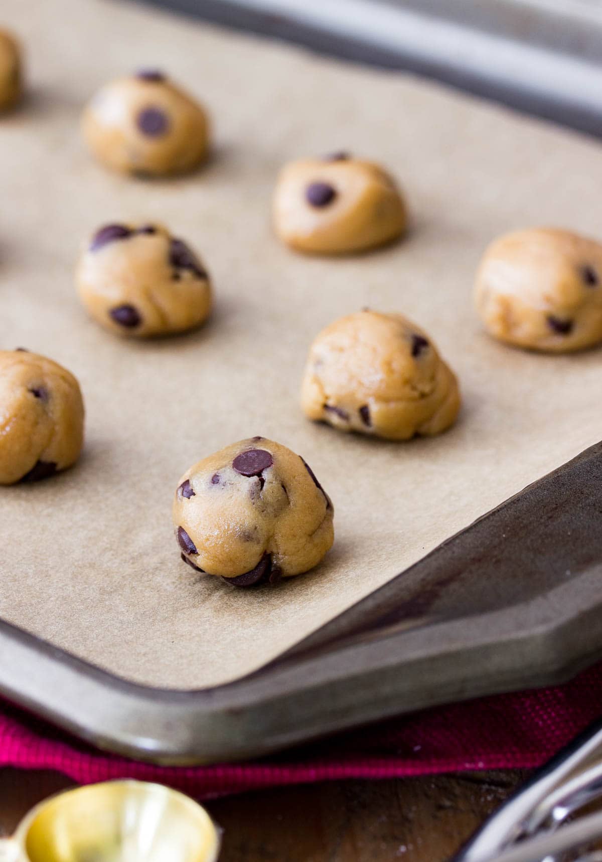 Tiny scoops of chocolate chip cookie dough on a parchment lined baking sheet.