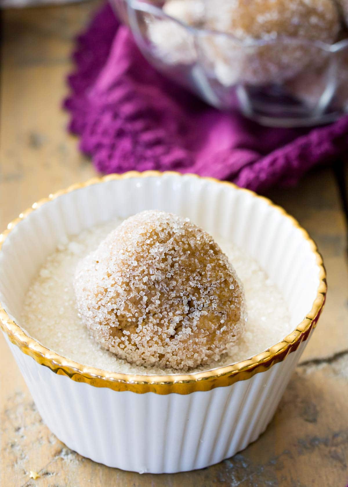 Cookie dough ball being rolled through coarse sugar before baking.