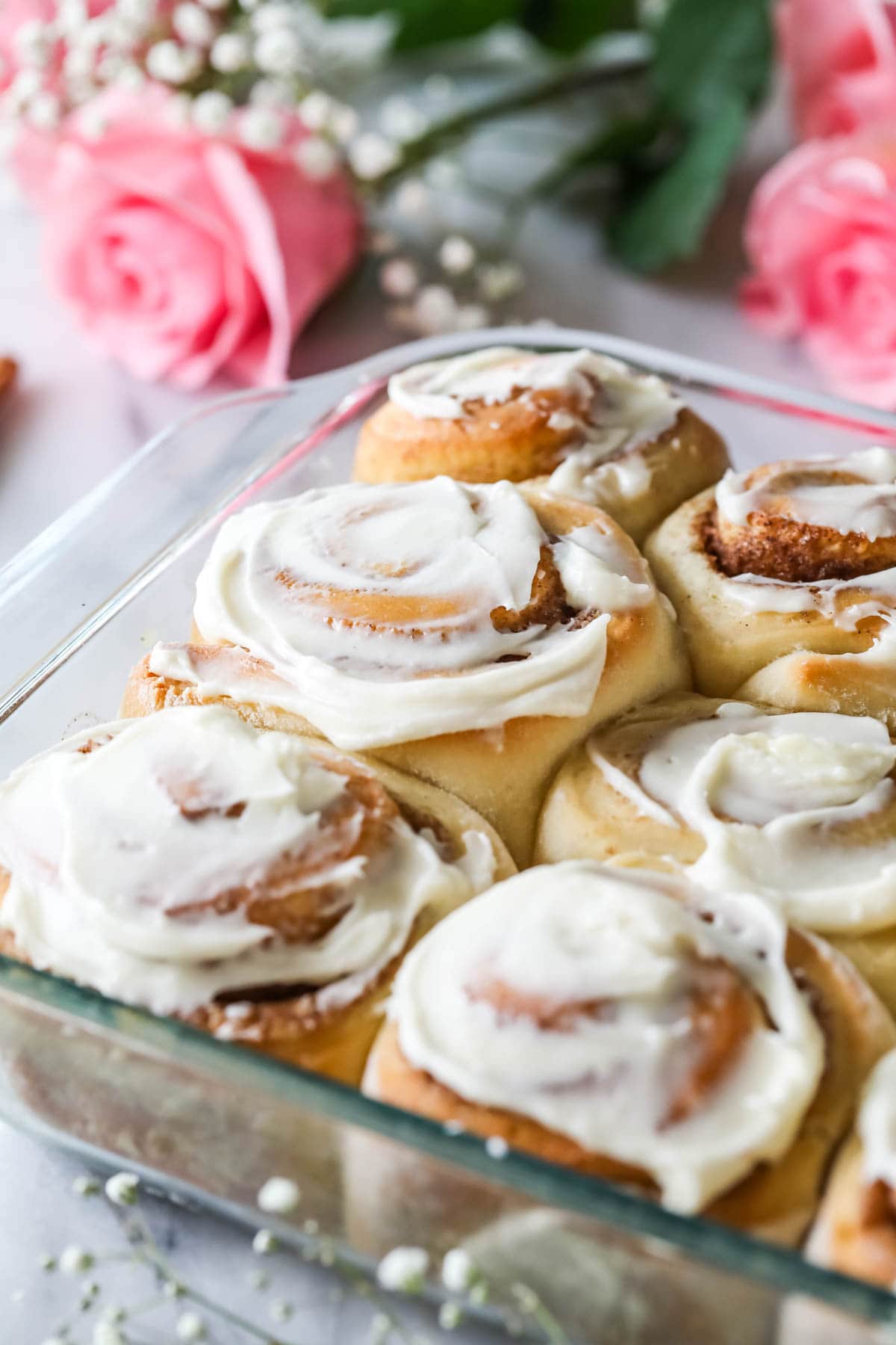 Glass dish of overnight cinnamon rolls frosted with cream cheese frosting.