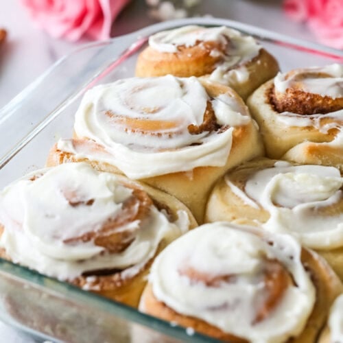 Glass dish of overnight cinnamon rolls frosted with cream cheese frosting.