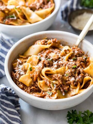 Two bowls of wide, long pasta noodles tossed in a shredded beef and tomato sauce.
