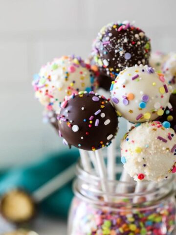Glass jar with chocolate and sprinkle coated cake balls on sticks.