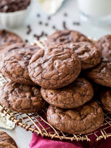Crinkly-topped flourless chocolate cookies stacked in a pile on a metal cooling rack.
