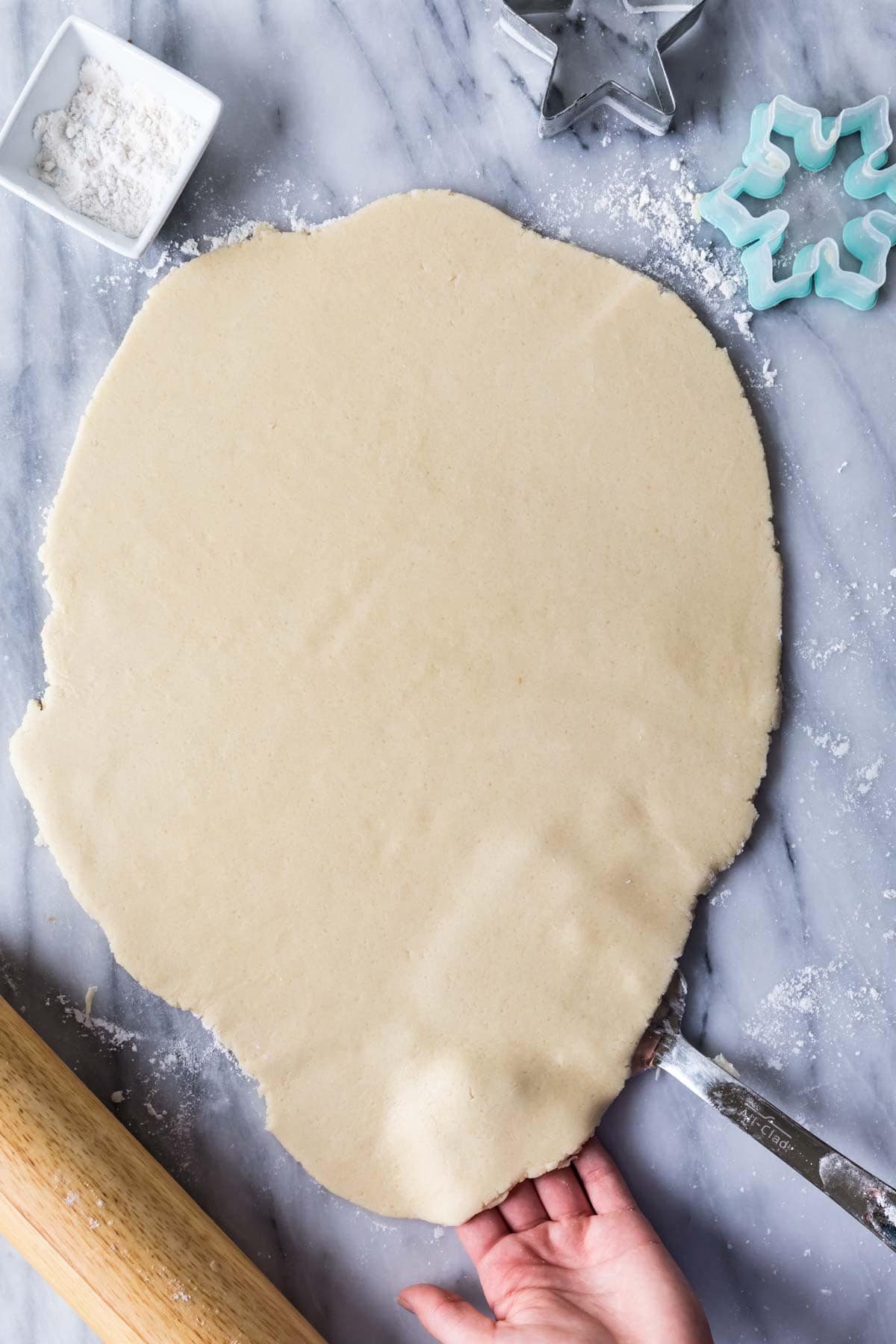 overhead of rolled out no-chill sugar cookie dough, showing how to use a spatula to lift the dough while you roll