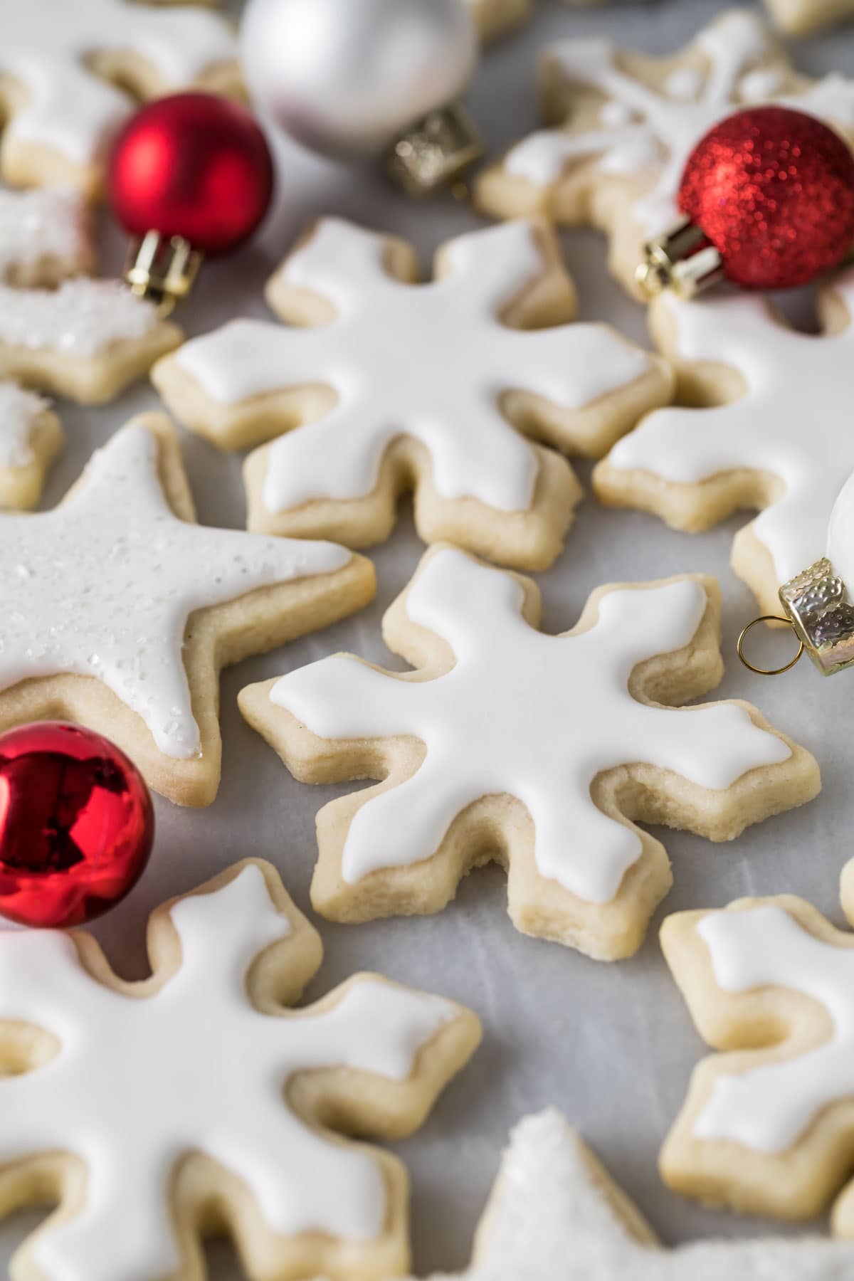 no-chill sugar cookies frosted with white icing and with red ornament balls in background