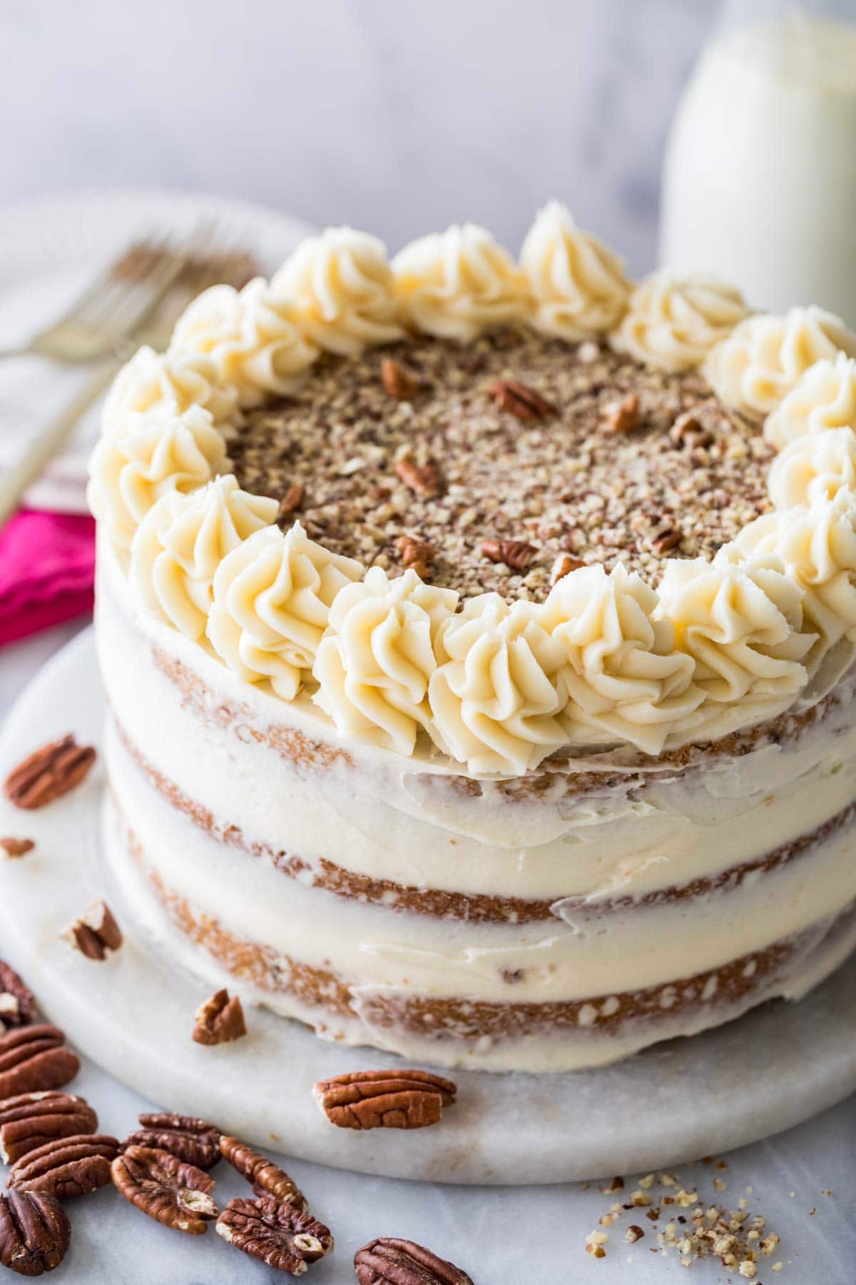Cake frosted naked style with finely chopped pecans and icing swirls on top.