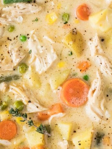 Close-up view of chicken pot pie soup with shredded chicken, carrots, potatoes, green beans, and other veggies.