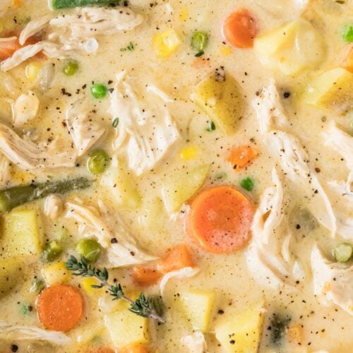 Close-up view of chicken pot pie soup with shredded chicken, carrots, potatoes, green beans, and other veggies.
