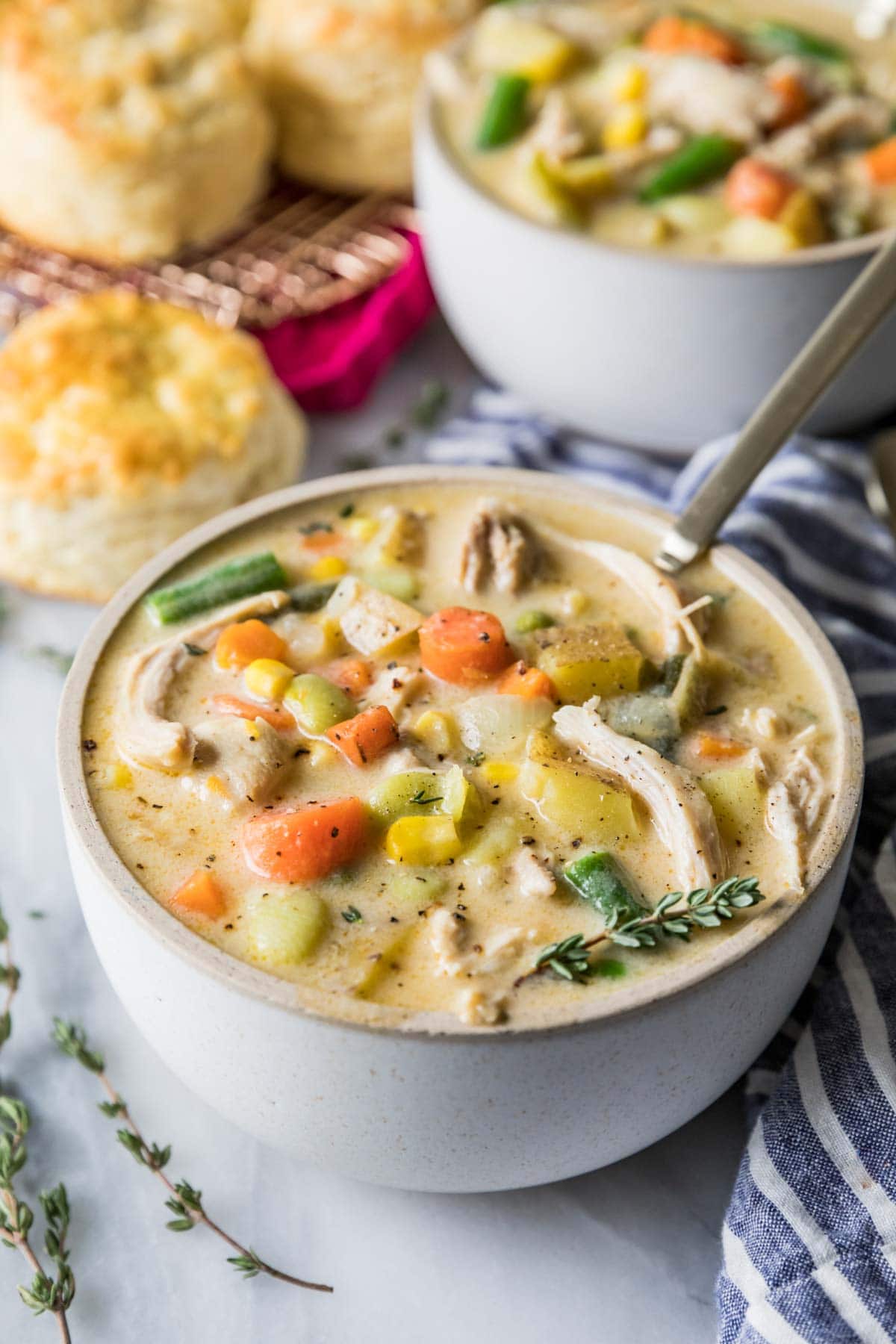 White bowl of chicken pot pie soup with mixed veggies and rotisserie chicken.