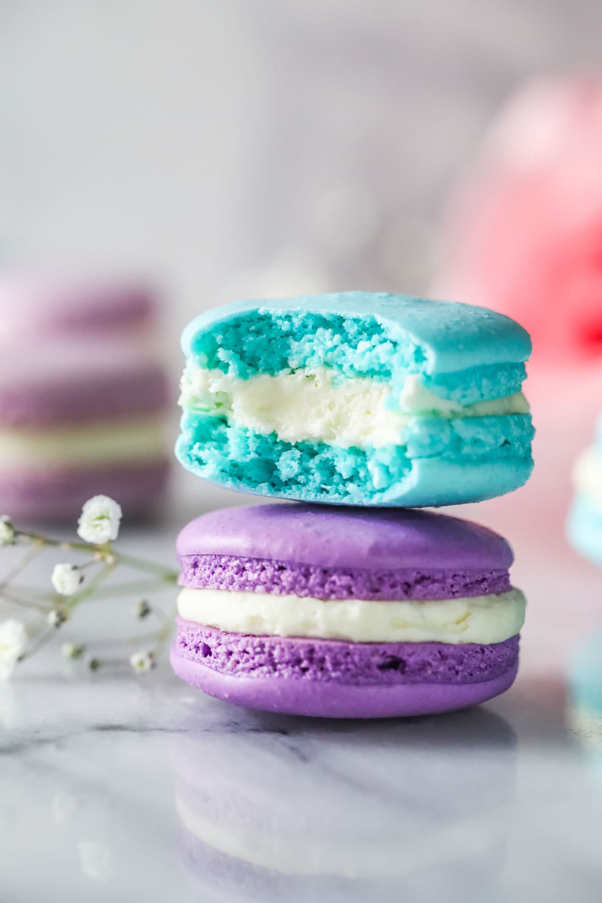 Blue macaron with a bite missing stacked on top of a purple French macaron