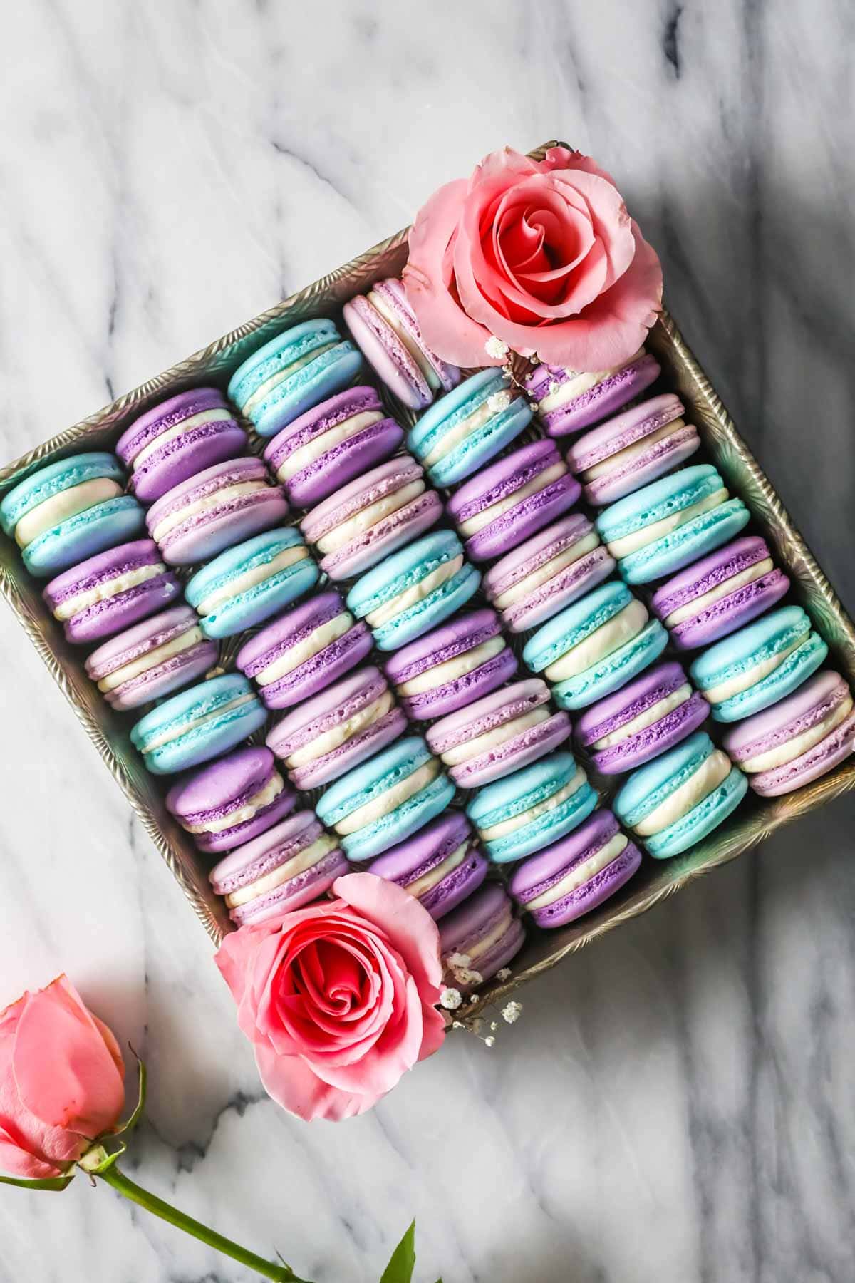 Blue, light purple, and dark purple macarons arranged in a square pan accented with large pink roses
