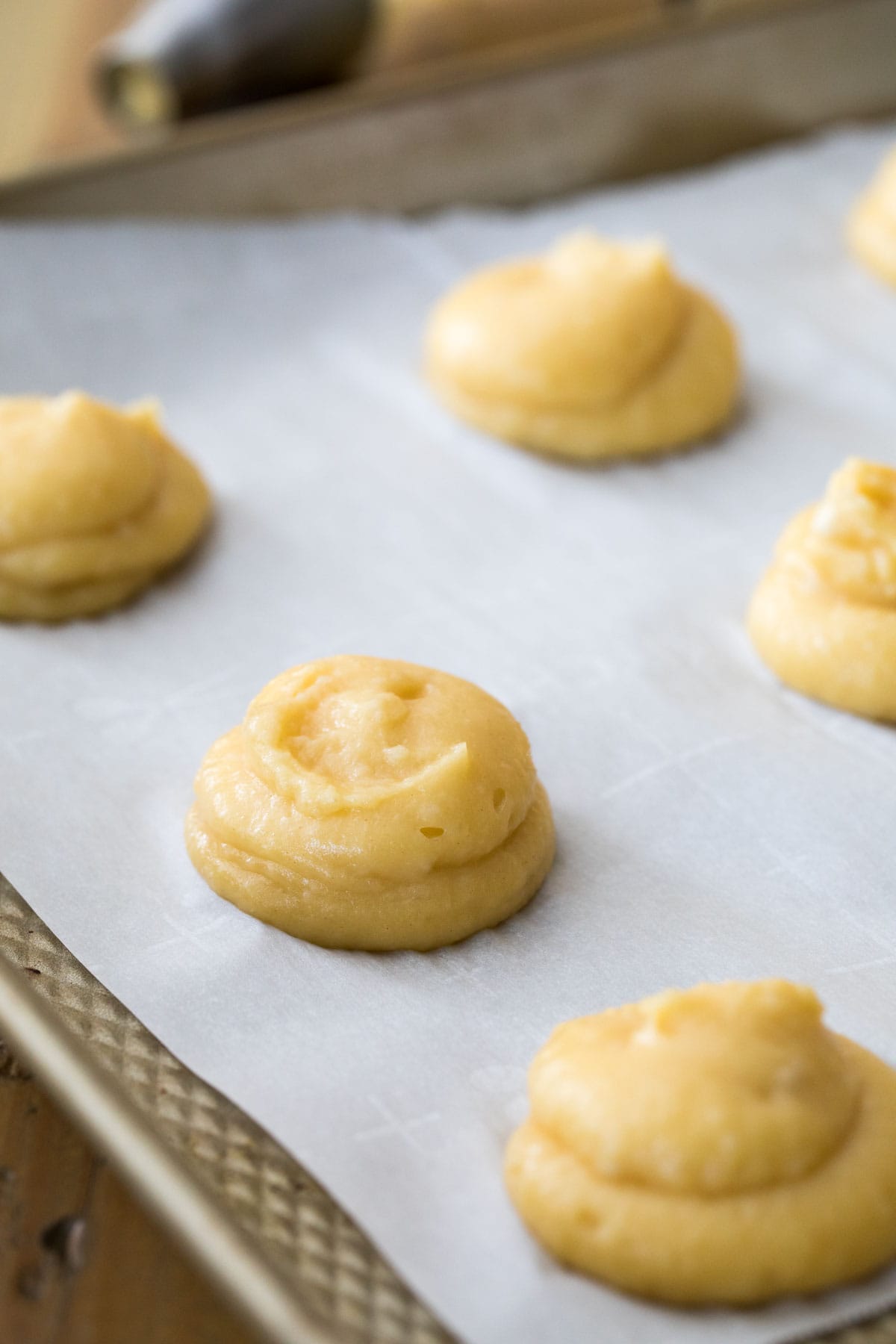 Choux dough that's been piped onto a baking sheet before baking.