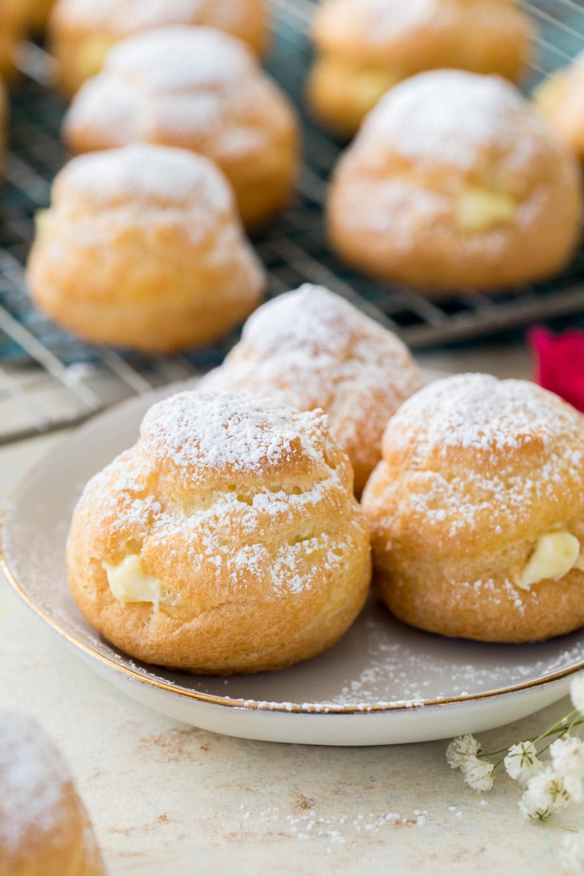 Plate of three custard-filled cream puffs dusted with powdered sugar.