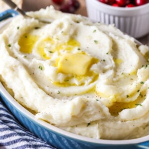 Oval shaped serving dish filled with mashed potatoes topped with melting butter.