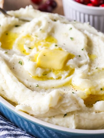 Oval shaped serving dish filled with mashed potatoes topped with melting butter.