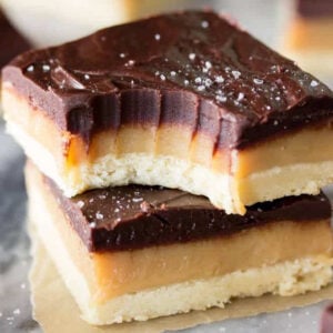 Two squares of millionaires shortbread stacked on top of each other with the top square missing one bite.