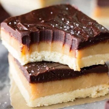 Two squares of millionaires shortbread stacked on top of each other with the top square missing one bite.