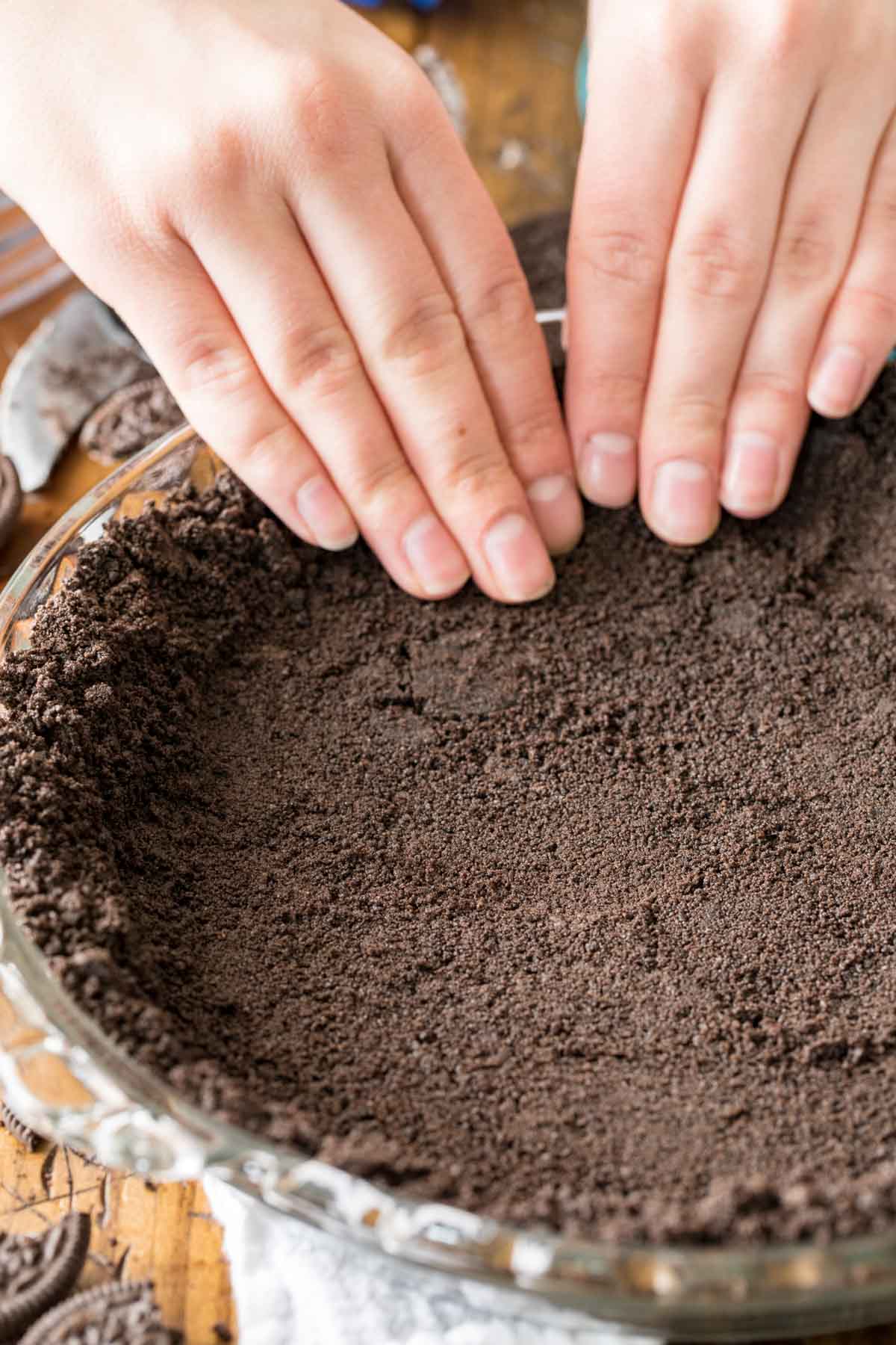 Hands pressing Oreo crumbs into a pie plate.